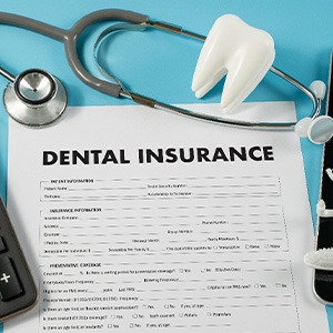A dental insurance form next to a calculator and some dental tools