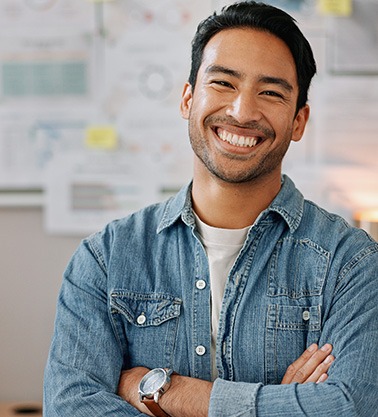 Man in denim jacket smiling with arms folded