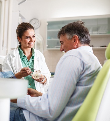 Smiling dentist showing patient model of teeth