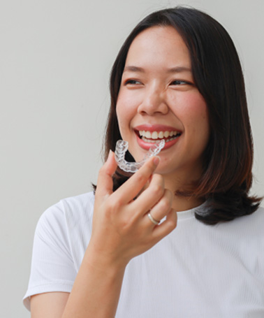Smiling patient holding clear aligner