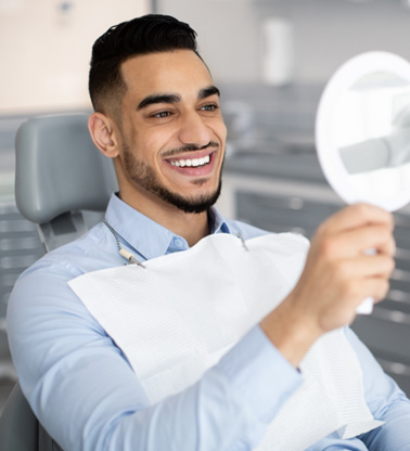Man smiling at reflection in handheld mirror
