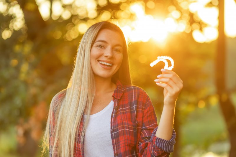 A smiling woman holding an aligner tray in an outdoor setting