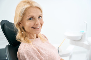 Woman in pink shirt sitting in dental chair and smiling